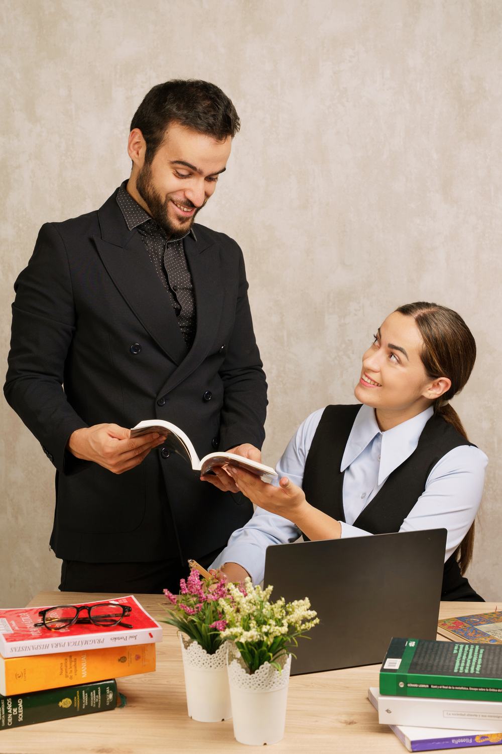 Abraham enseña un libro a Raquel en una mesa de estudio con flores y libros